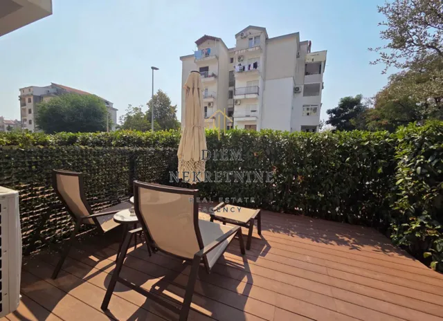 Terrace with wooden decking, sun loungers, and a view of the building and greenery.