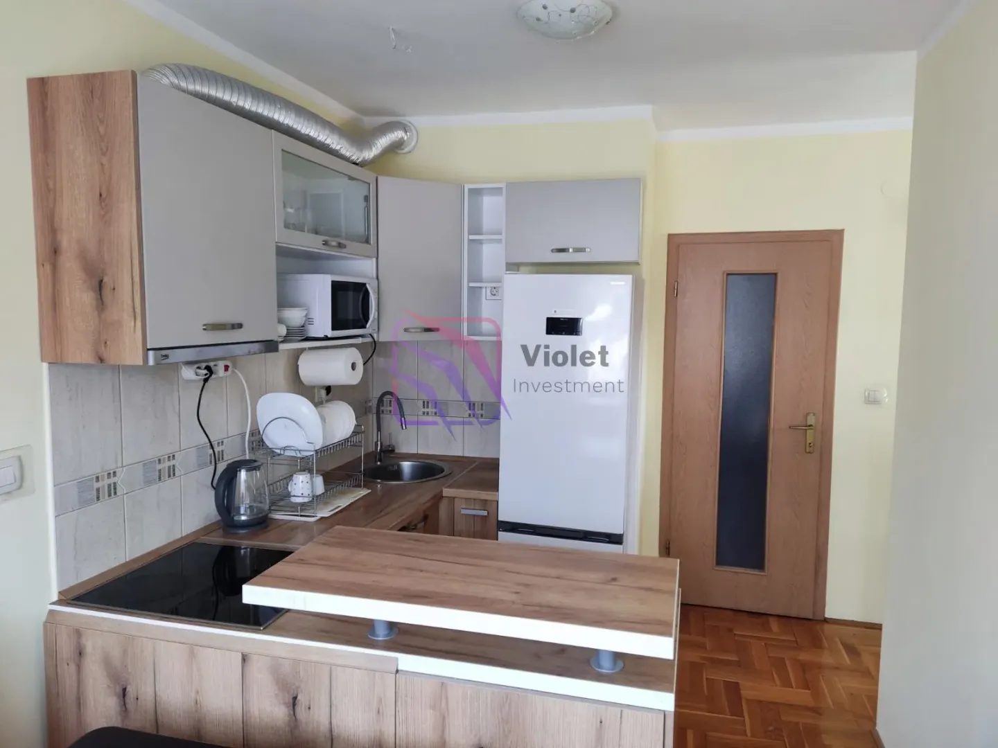 Manja kuhinja sa svijetlim elementima, bijelim frižiderom i drvenim šankom.