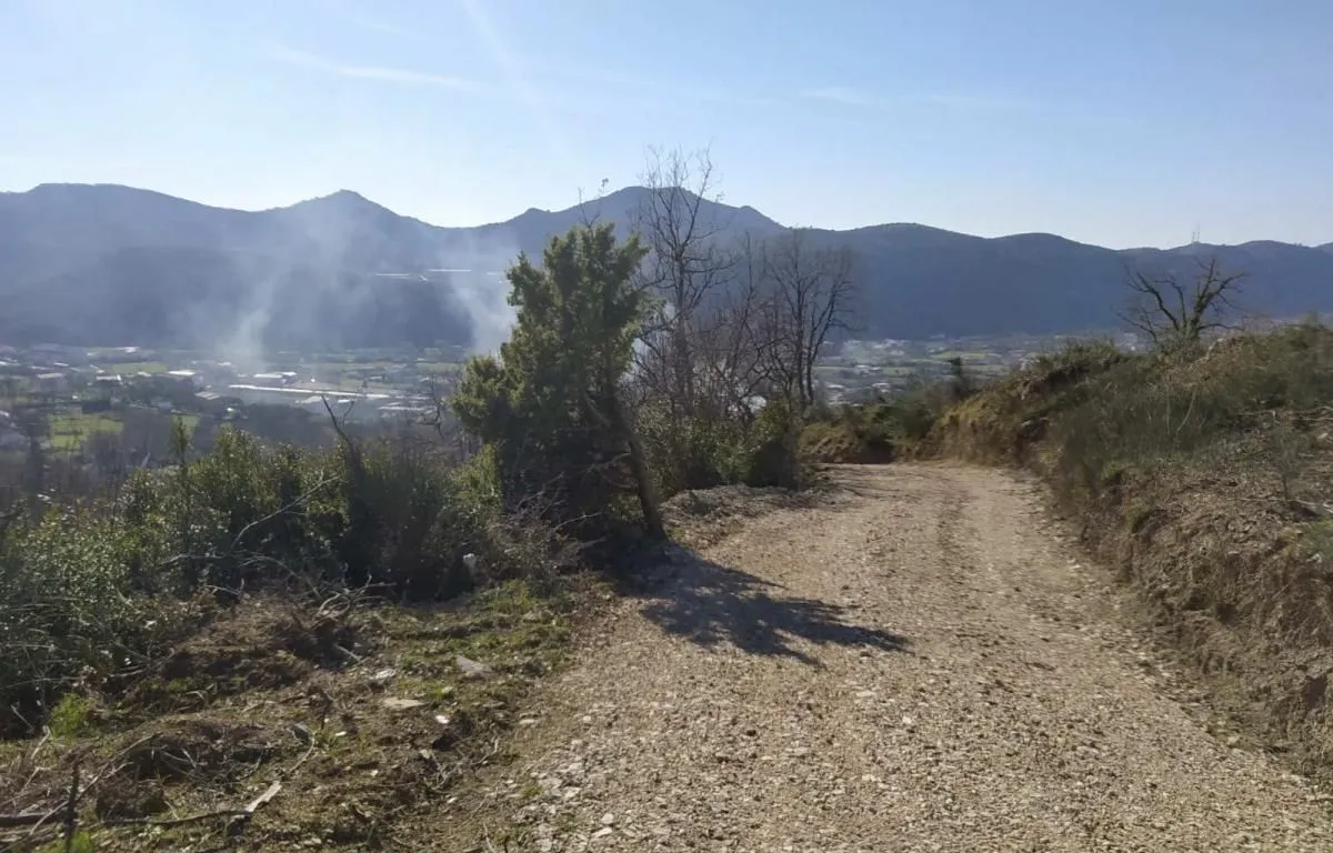 Zemljani put koji vodi kroz prirodu sa pogledom na brda i okolinu.