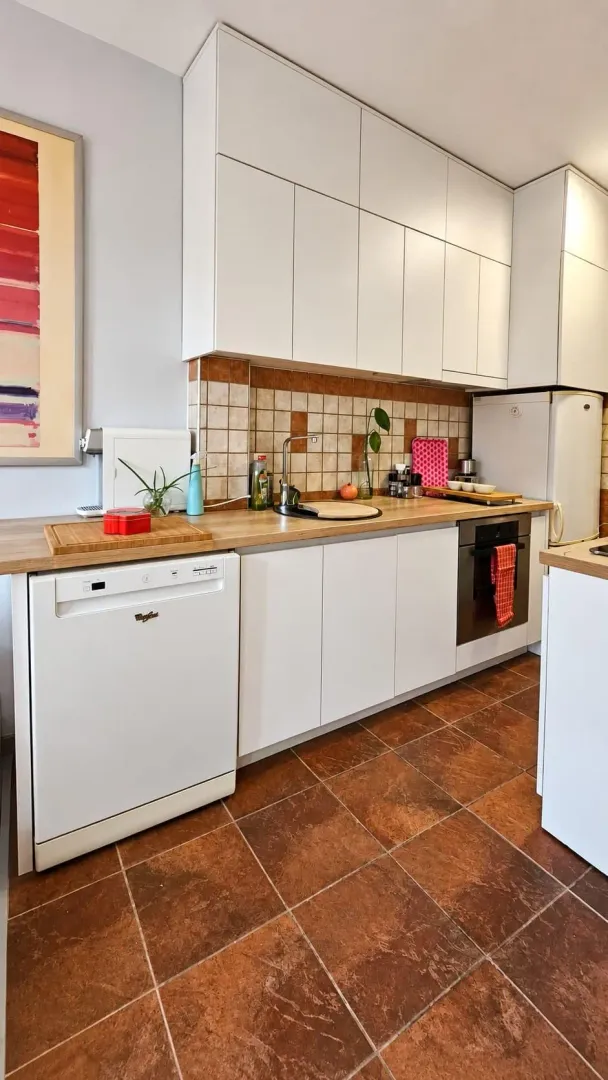 Small bright kitchen with white cabinetry, wooden countertop, and tiled floor.