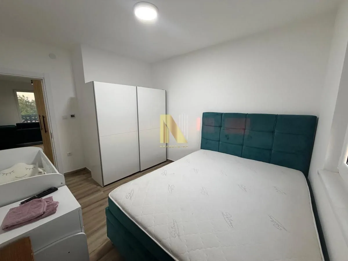 Nameštena spavaća soba sa bračnim krevetom, belim garderoberom i krevetcem za bebe.
