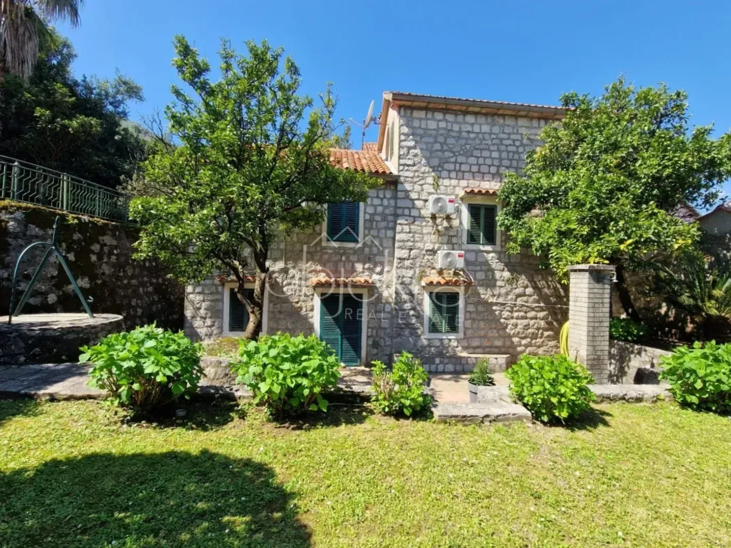 View of a stone house with a yard and greenery.