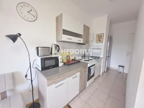 Manja kuhinja sa drvenim elementima, belom radnom površinom i šporetom. - image 6