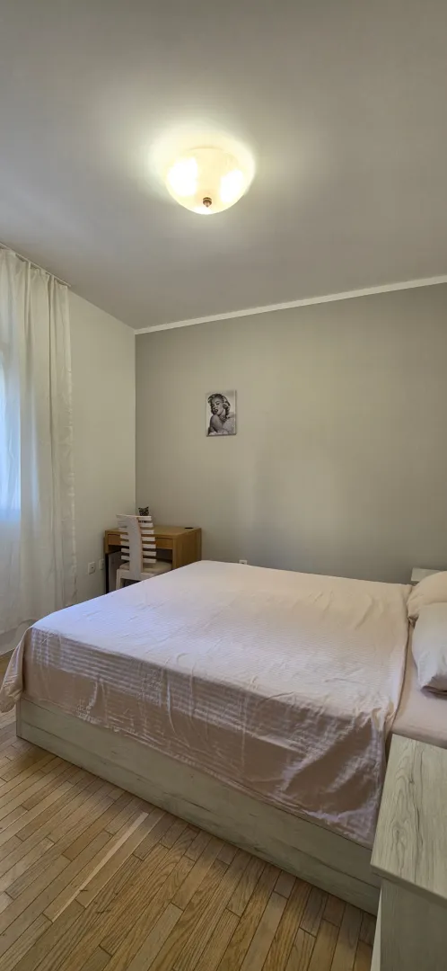 Spavaća soba sa bračnim krevetom, radnim stolom i drvenim podom.