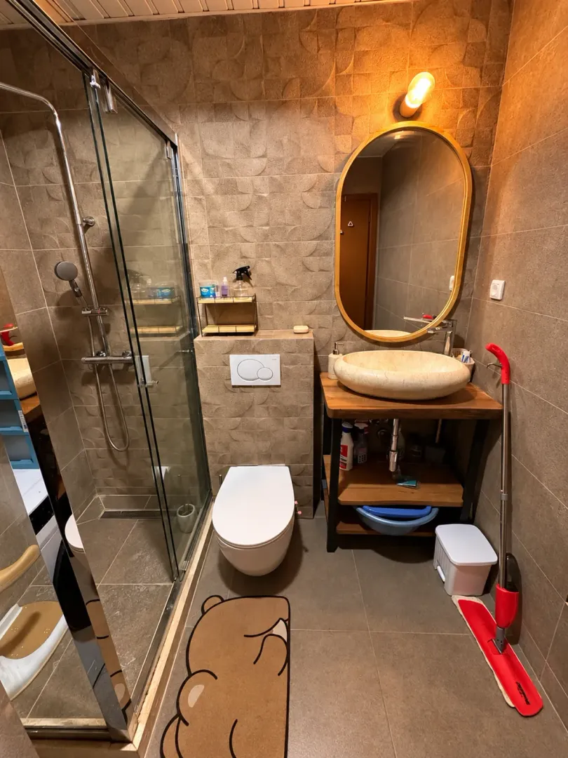 Manje uređeno kupatilo sa tuš kabinom, umivaonikom i wc šoljom.