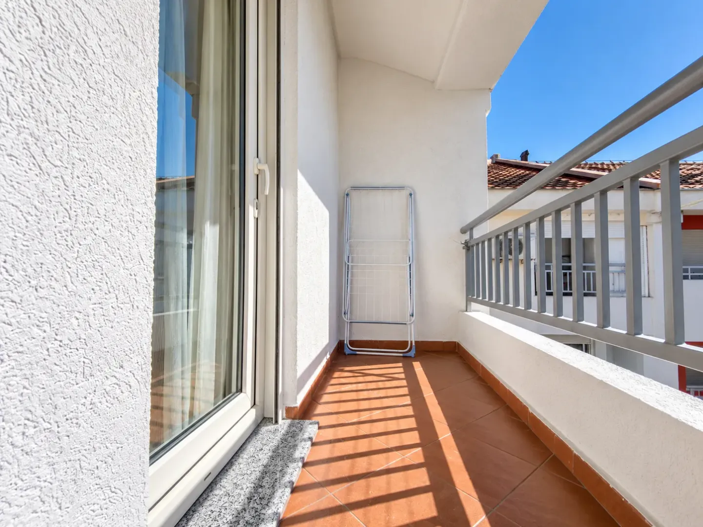 Balkon sa popločanim podom, metalnom ogradom i sušačem za veš.