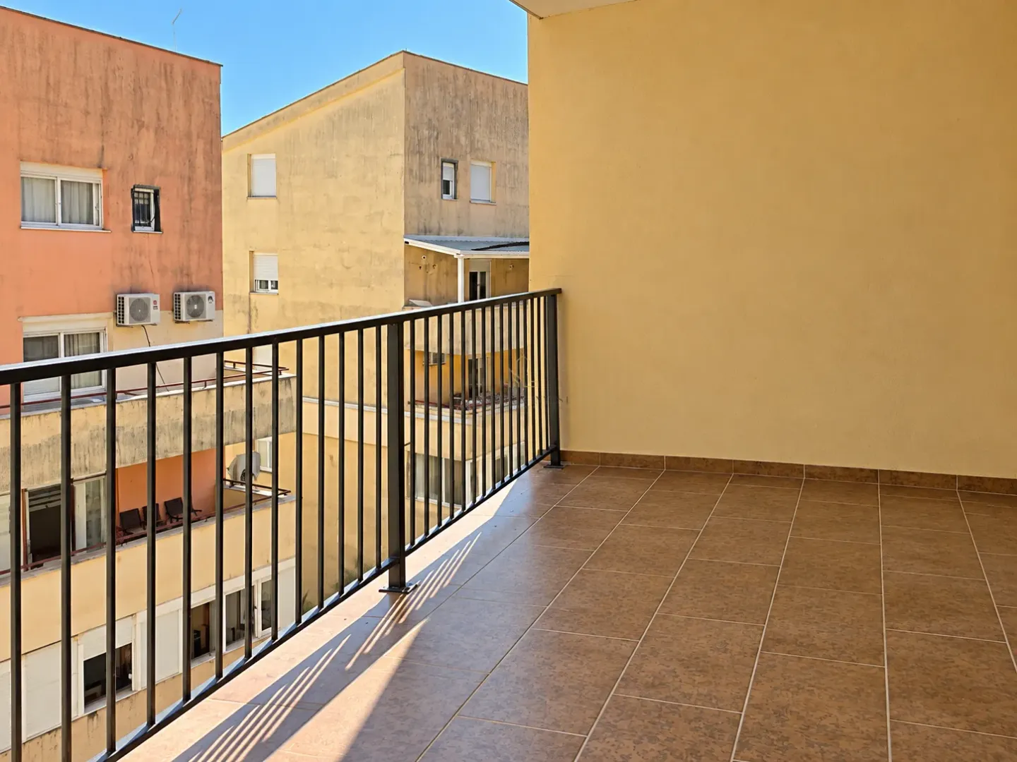 Nenamešten balkon sa keramičkim pločicama i pogledom na okolne zgrade.