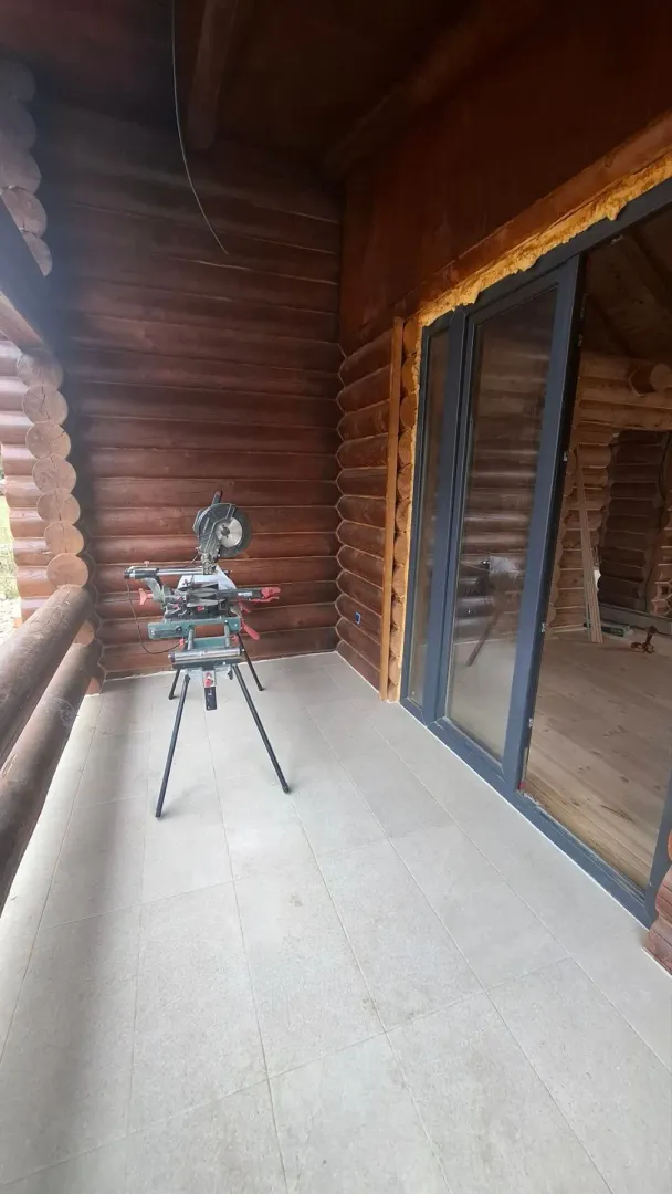 Covered terrace of a wooden cottage with a cutting saw set up.