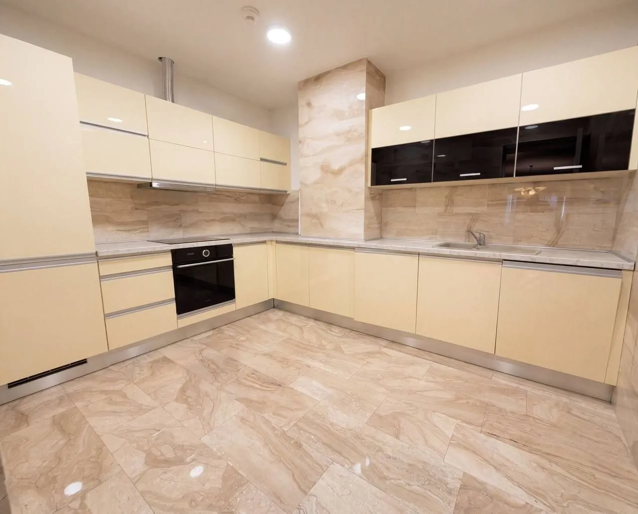 Modern kitchen with beige cabinets and marble tile flooring.