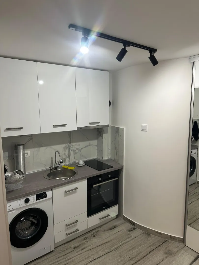 Small white kitchen with a sink, built-in oven, and washing machine.