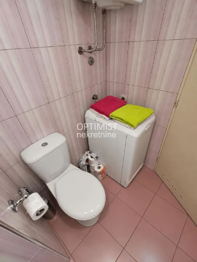 Manje kupatilo sa wc šoljom, veš mašinom i pločicama na zidovima.