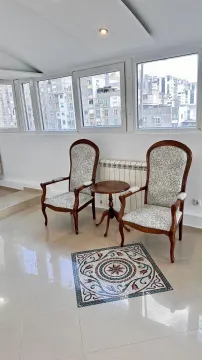 A corner arranged with two armchairs and a small table by large windows with a city view. - image 4