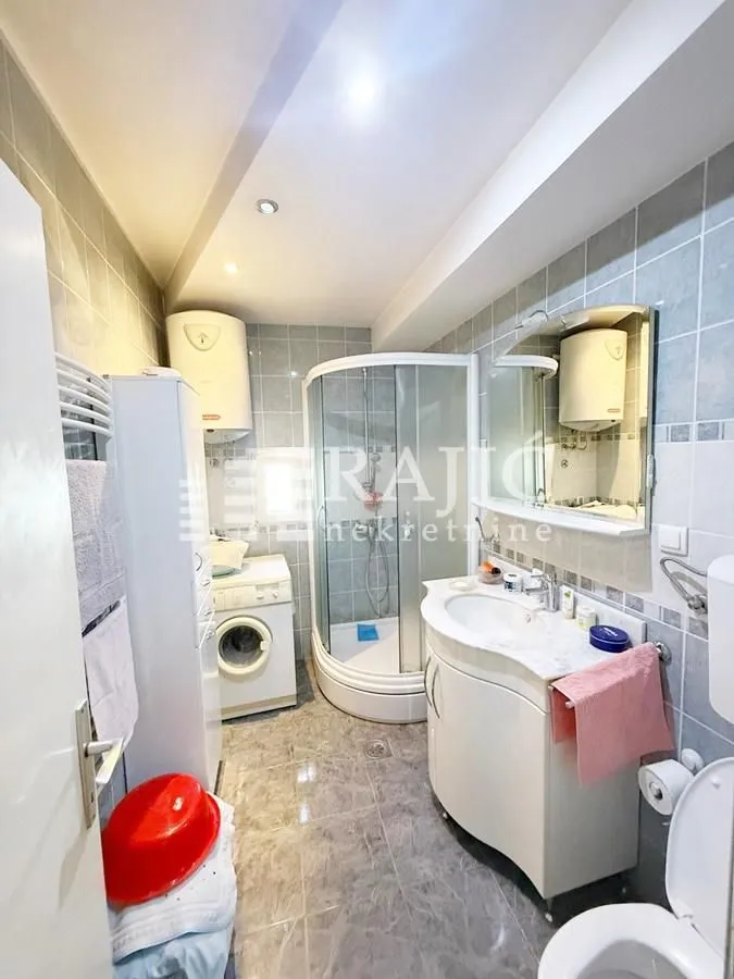 Smaller bathroom with a shower cabin, sink, washing machine, and toilet.