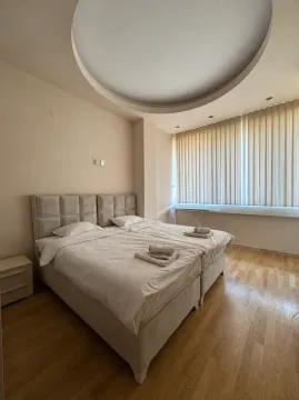 Prostrana spavaća soba sa bračnim krevetom, drvenim podom i velikim prozorom sa zavjesama. - image 9