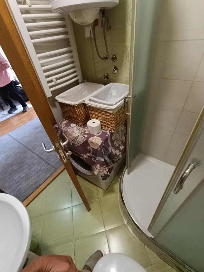 Pogled na kupatilo sa tuš kabinom, bojlerom i korpama za veš.