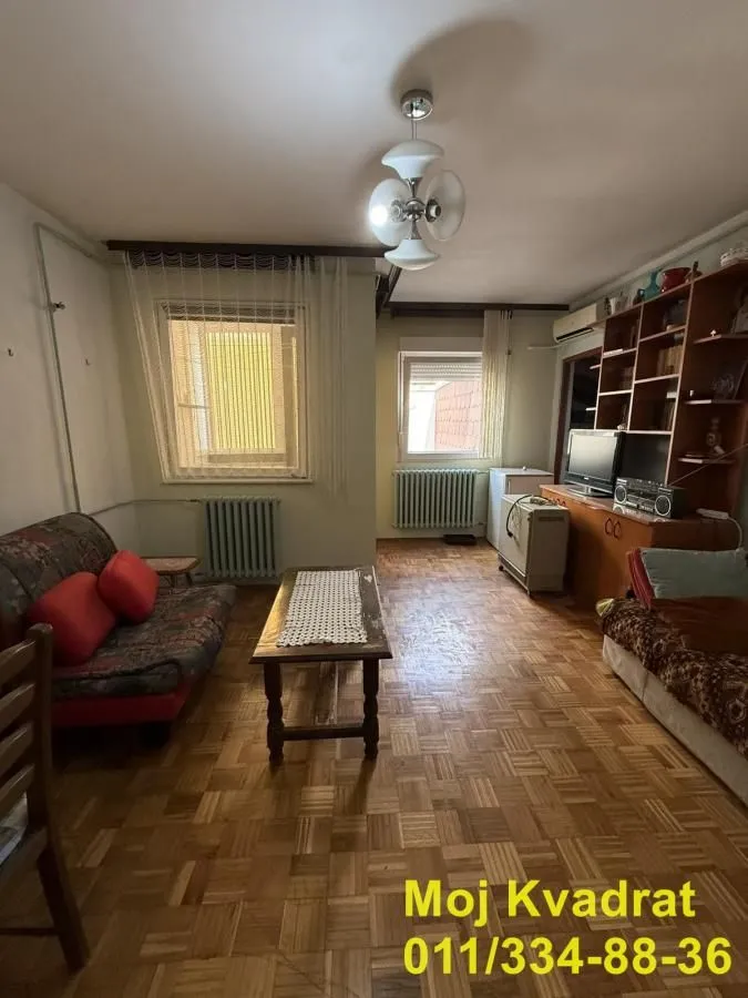 Dnevna soba sa garniturom za sedenje, drvenim podom i policama za knjige.