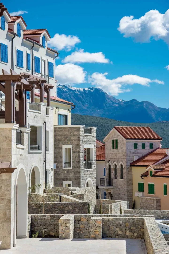 Pogled na arhitekturu zgrada sa kamenom fasadom i planinama u pozadini.