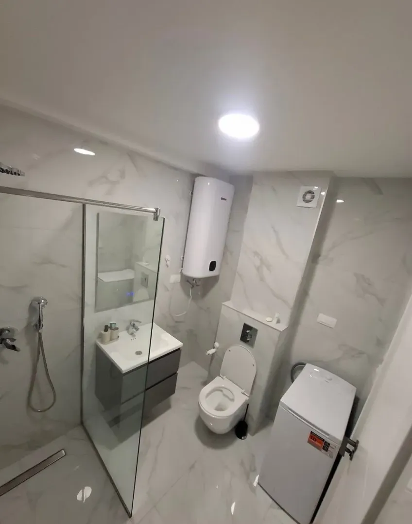 Modernly equipped bathroom with a shower cabin, sink, and washing machine.