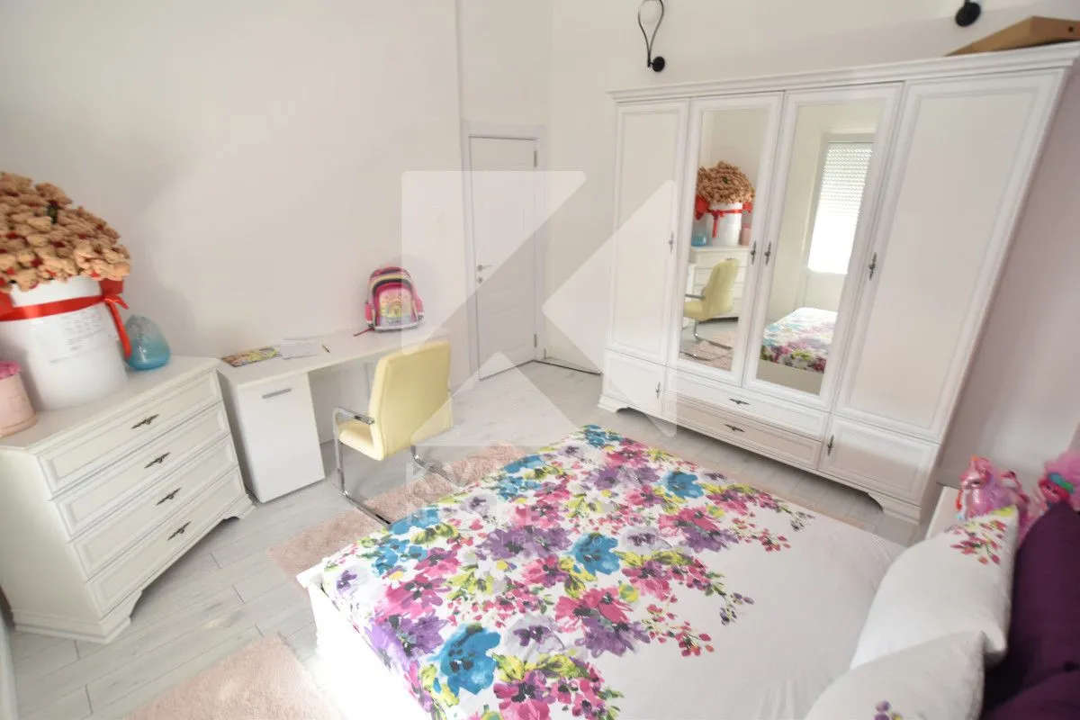 Children's bedroom with a bed, white wardrobe, desk, and chest of drawers.