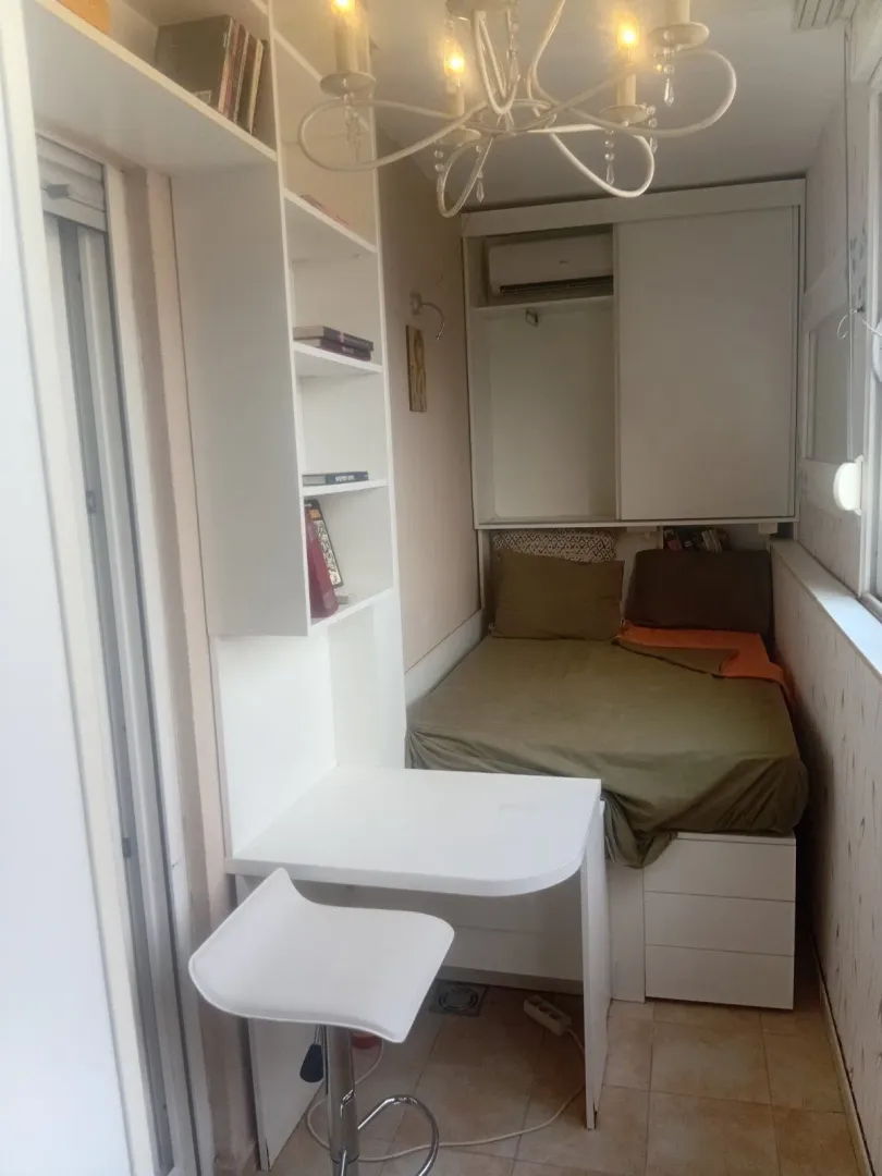 Manja opremljena spavaća soba sa krevetom, radnim stolom i policama.