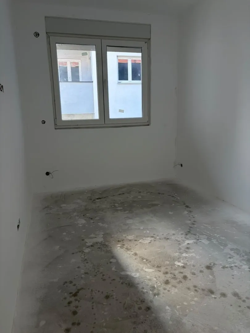 Prazna neuređena prostorija sa belim zidovima i prozorom.
