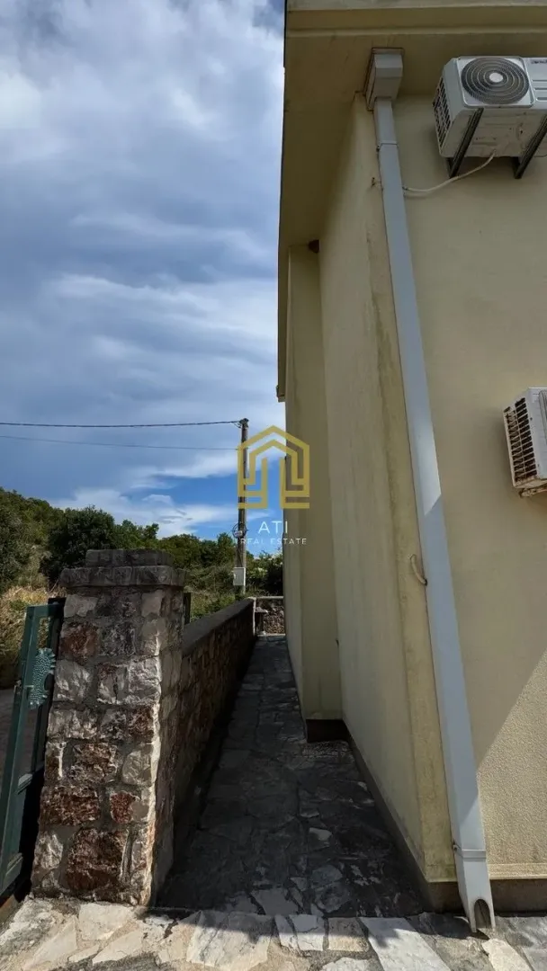 Bočna fasada kuće sa prolazom i kamenom stazom.
