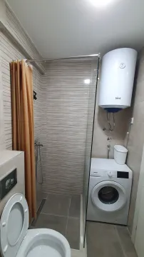 Compact bathroom with a shower cabin, toilet, and washing machine. - image 9
