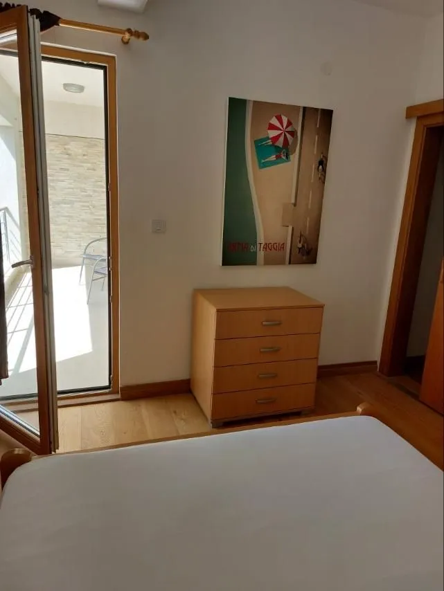 Svijetla spavaća soba sa komodom i izlazom na balkon.