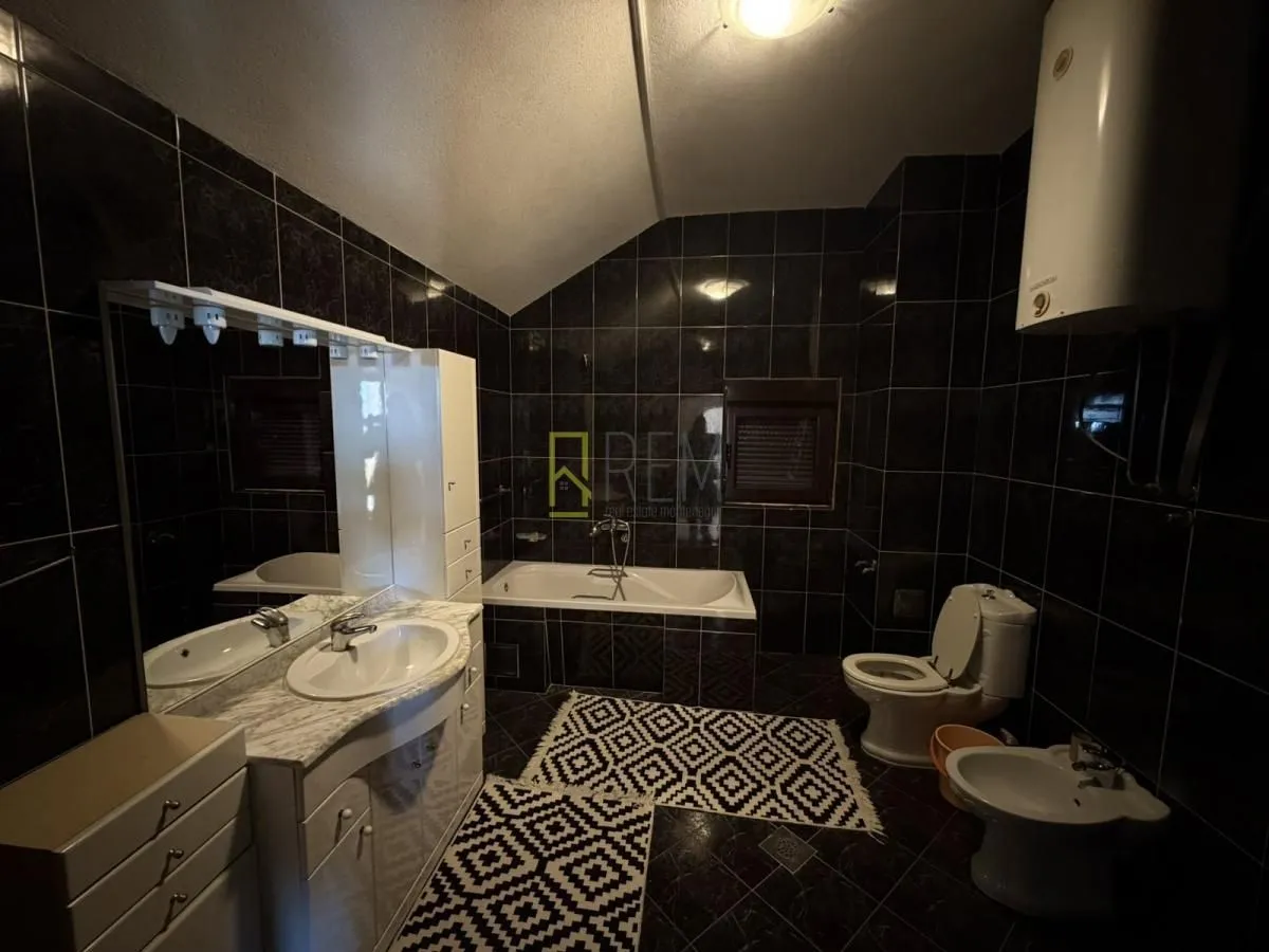 Fully equipped bathroom with bathtub, sink and black tiles.