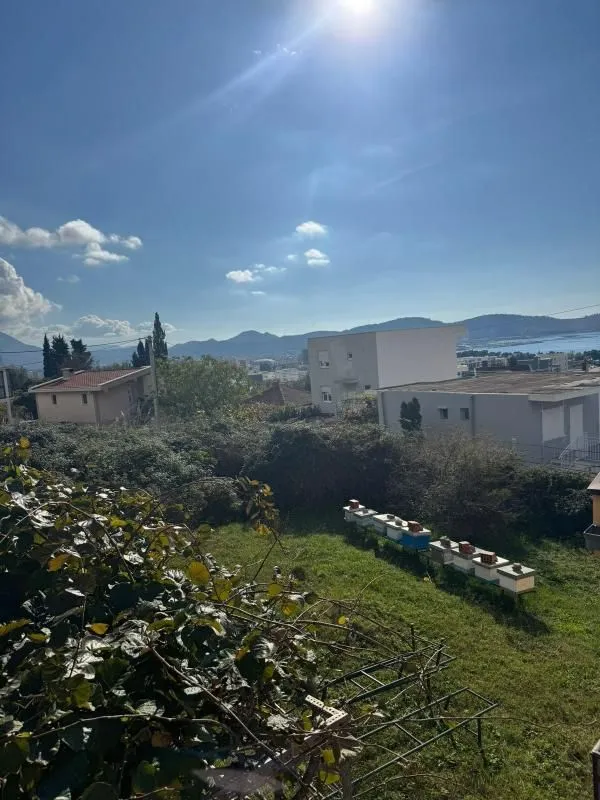 Pogled iz dvorišta na okolne kuće, brda i plavo nebo.