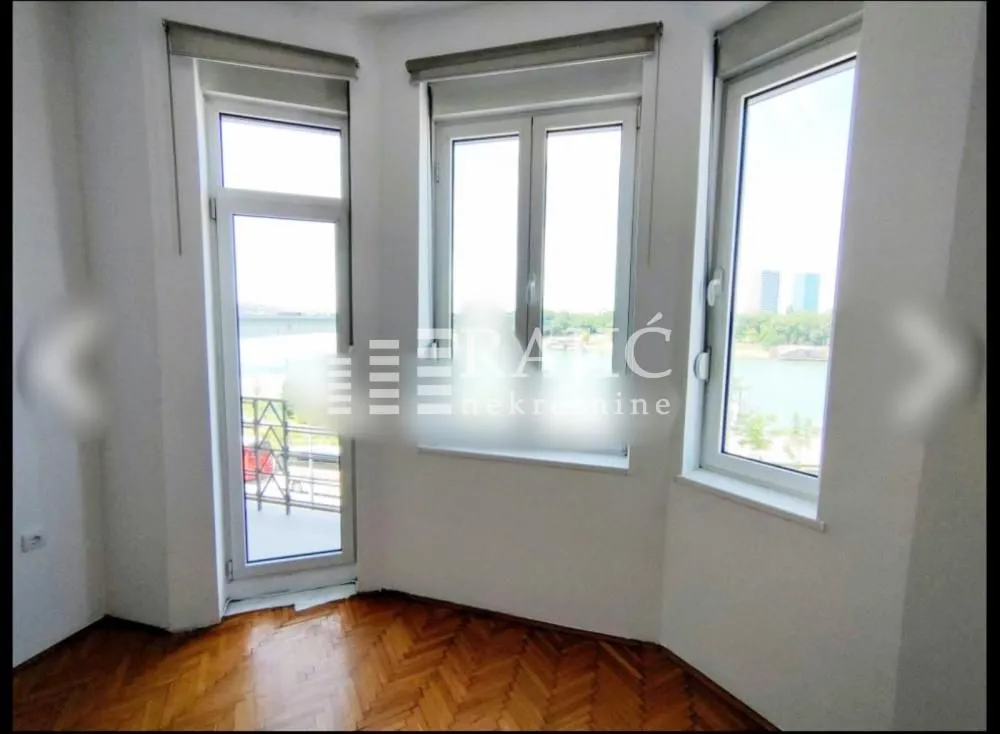 Empty room with parquet flooring and large windows offering a river view.