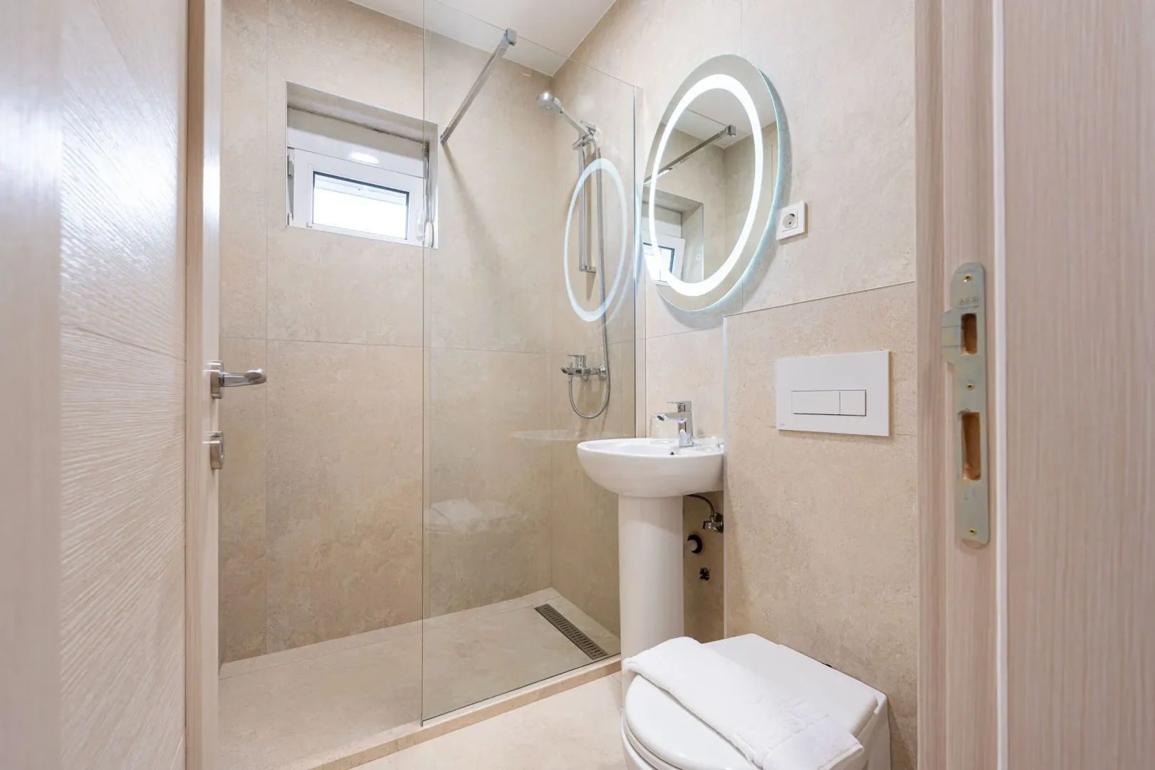 Modern bathroom with a walk-in shower, washbasin, and illuminated mirror.