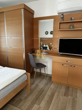 Furnished bedroom with a wooden wardrobe, desk, and TV. - image 14