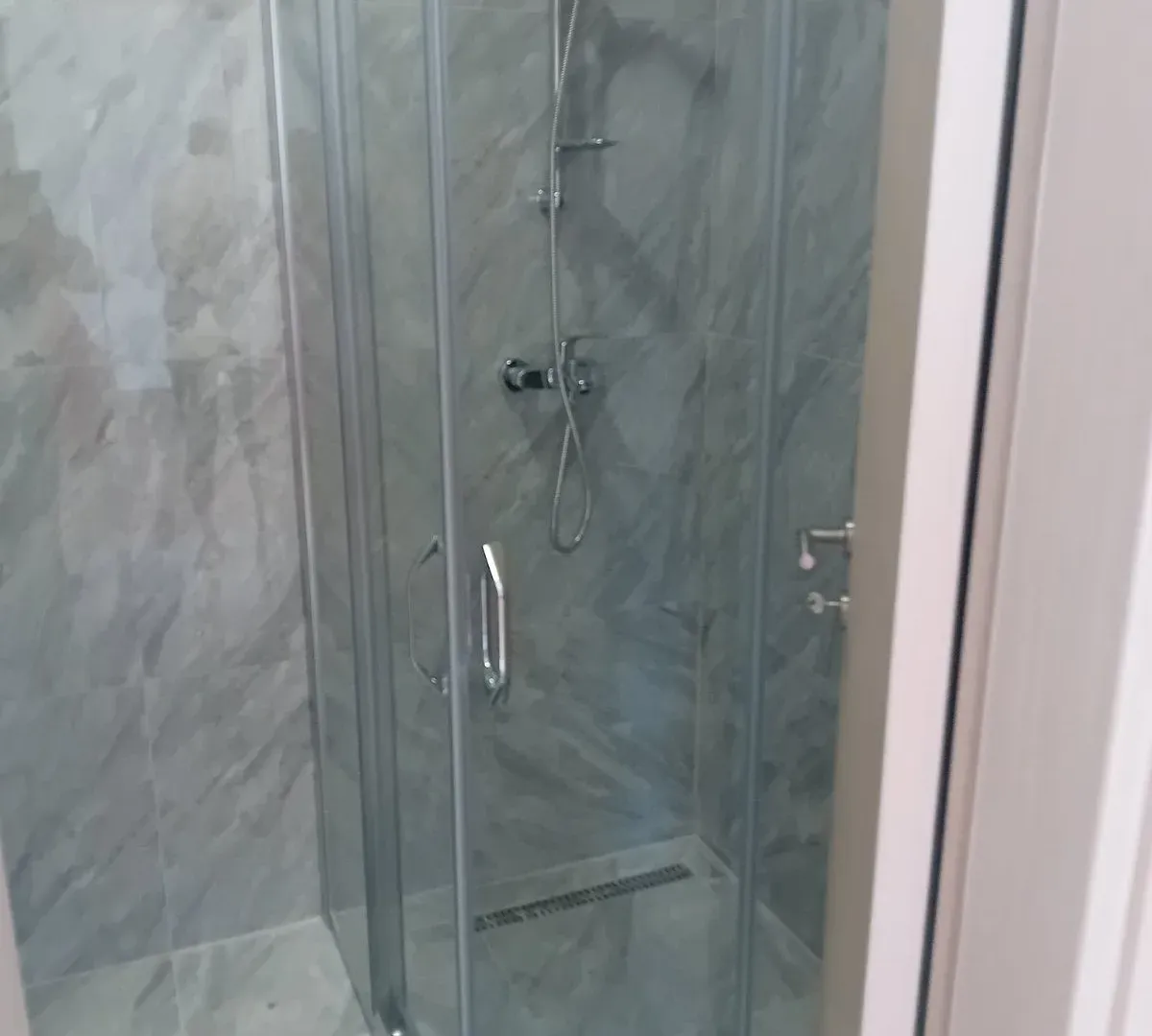 Bathroom with a glass shower enclosure and grey tiles.