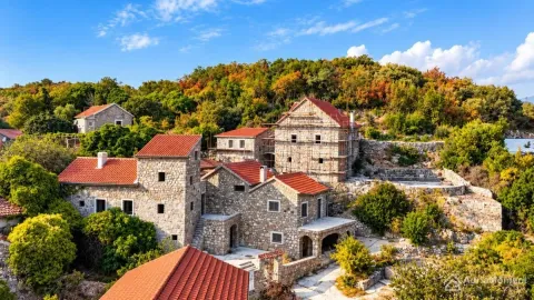 Pogled iz vazduha na kamene kuće sa crvenim krovovima u izgradnji okružene zelenilom. - image 2