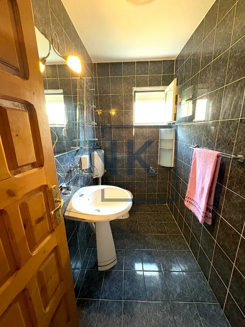 Bathroom tiled in dark tiles with a washbasin and mirror.