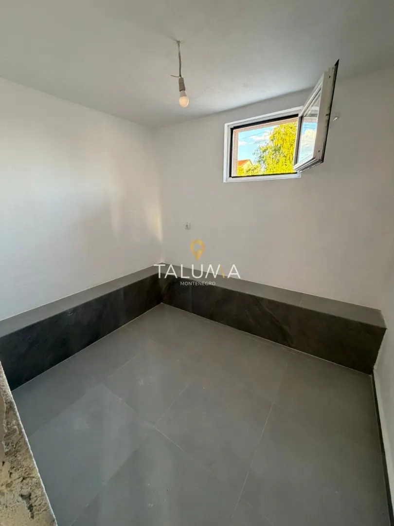Empty room with white walls, grey floor tiles, and a window with an outside view.