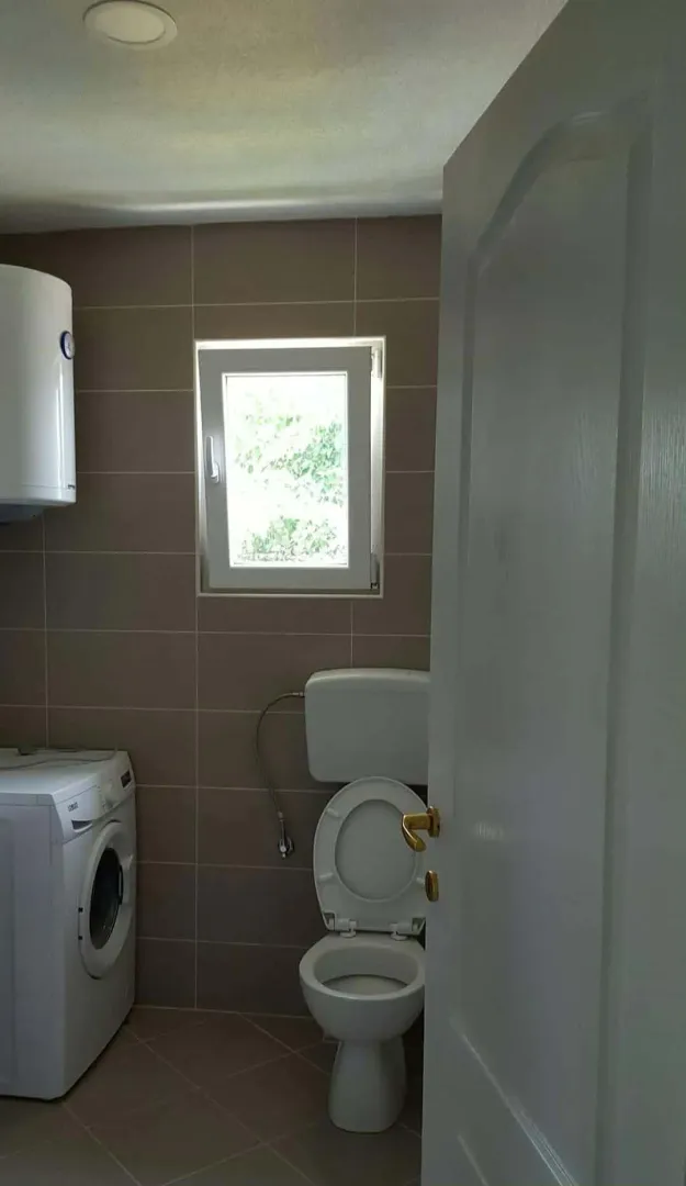 Pogled na kupatilo sa wc šoljom, mašinom za veš i bojlerom.