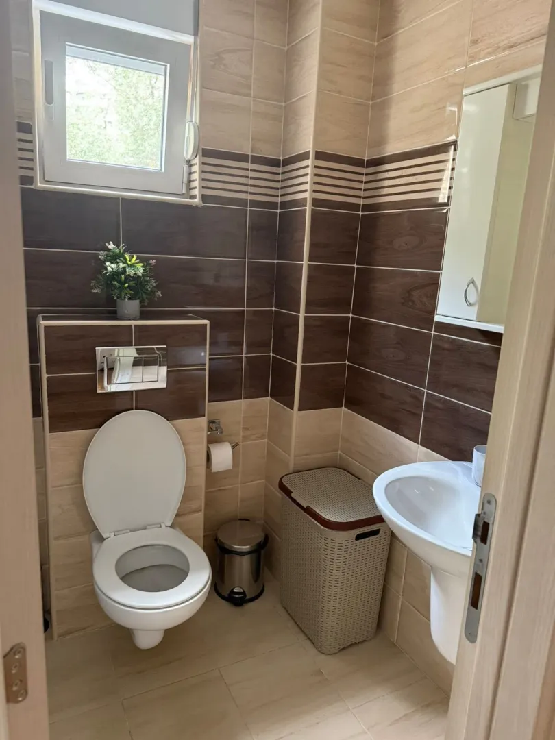 Manje kupatilo sa WC šoljom, umivaonikom i pločicama u braon tonovima.