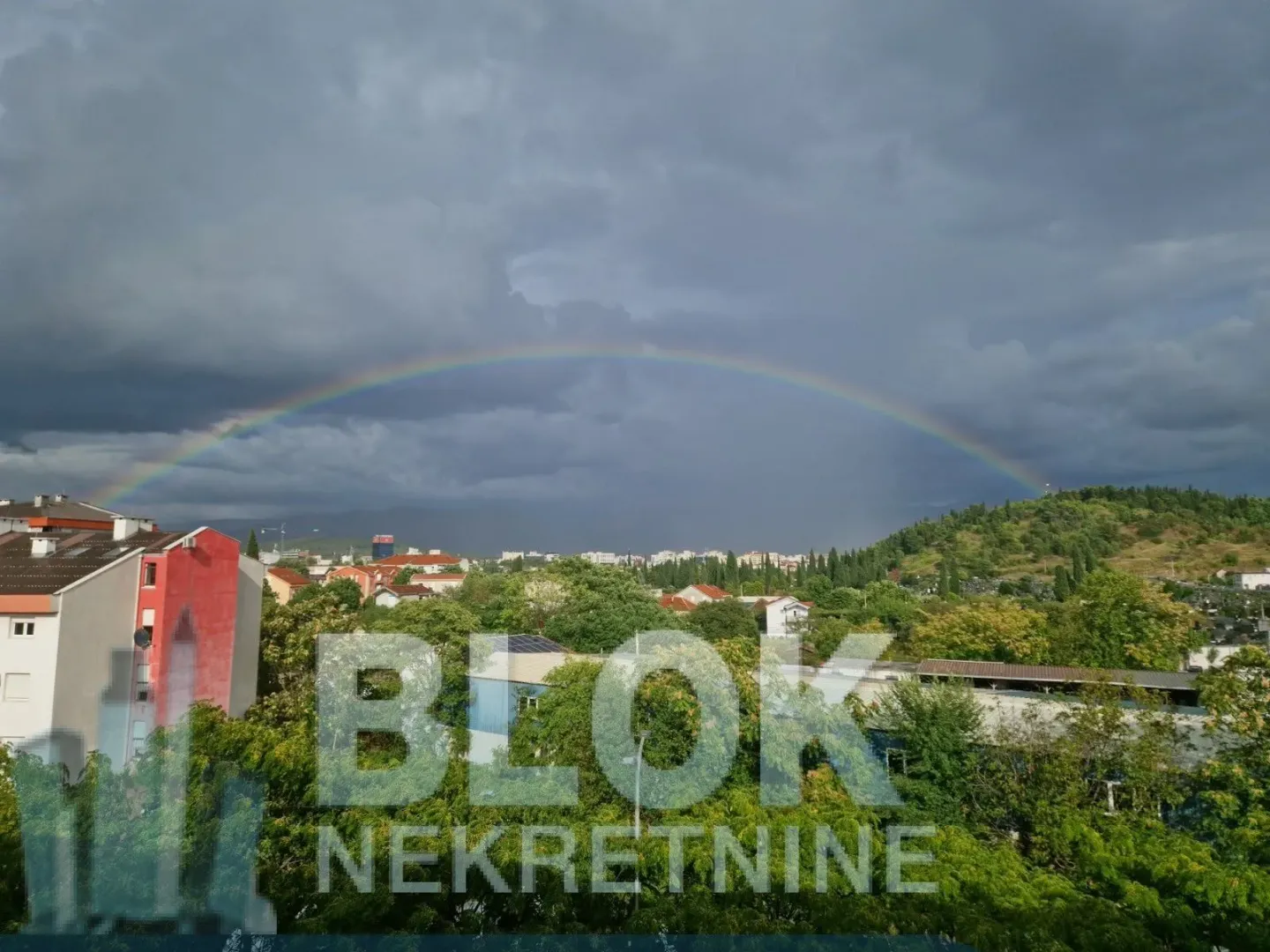 View from the apartment overlooking the cityscape with a rainbow and cloudy sky.