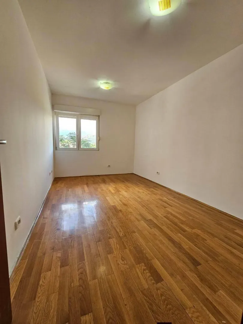 Prazna soba sa parketom i prozorom koji gleda spolja.