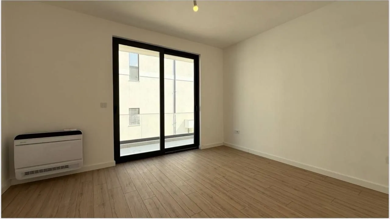 Empty unfurnished room with laminate flooring and balcony doors.