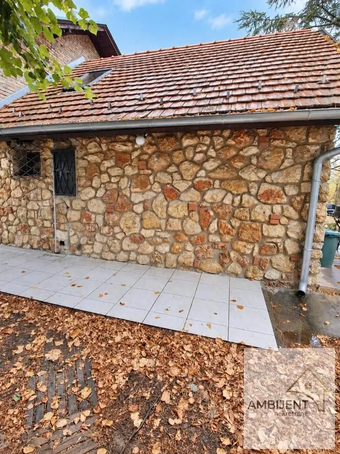 Pogled na spoljni deo kuće sa kamenom fasadom i popločanim dvorištem.