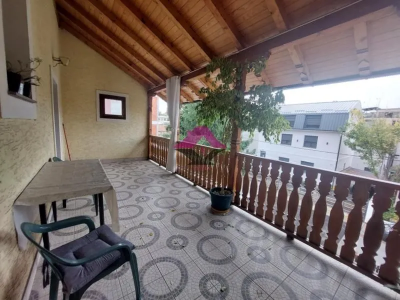 Natkrivena terasa sa drvenom ogradom, podnim pločicama i garniturom za sedenje.