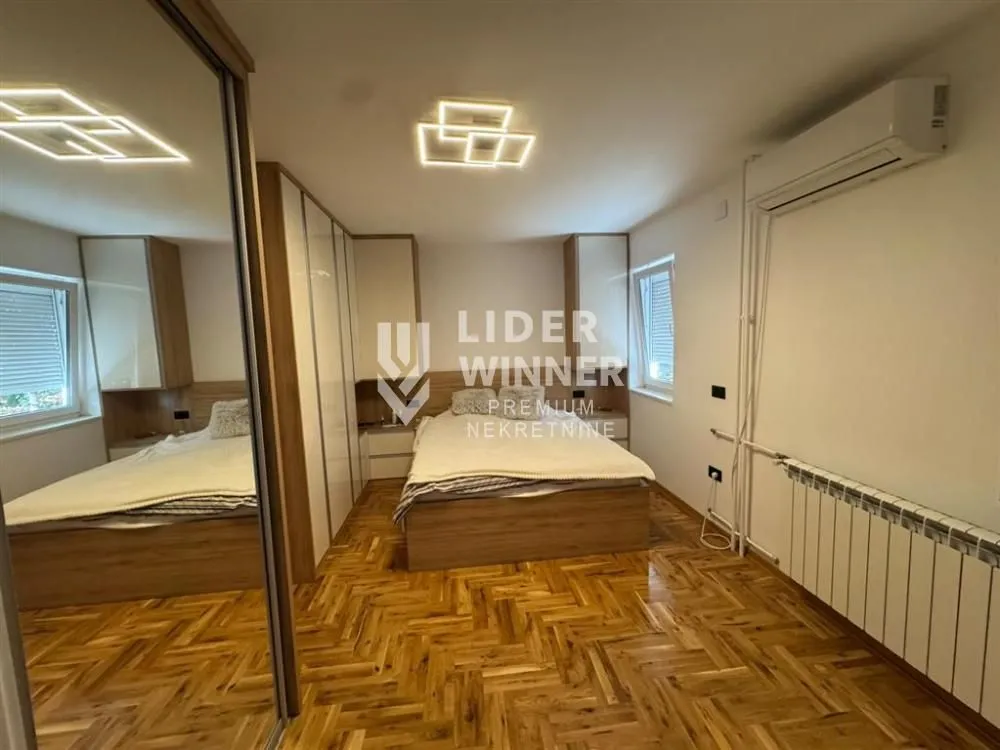 Nameštena spavaća soba sa bračnim krevetom, ugradnim ormarima i drvenim podom.