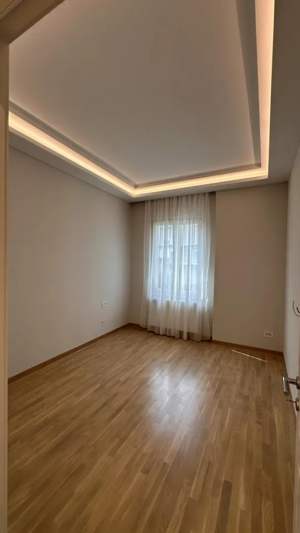 Empty room with wooden flooring, a window, and a dropped ceiling with lighting.