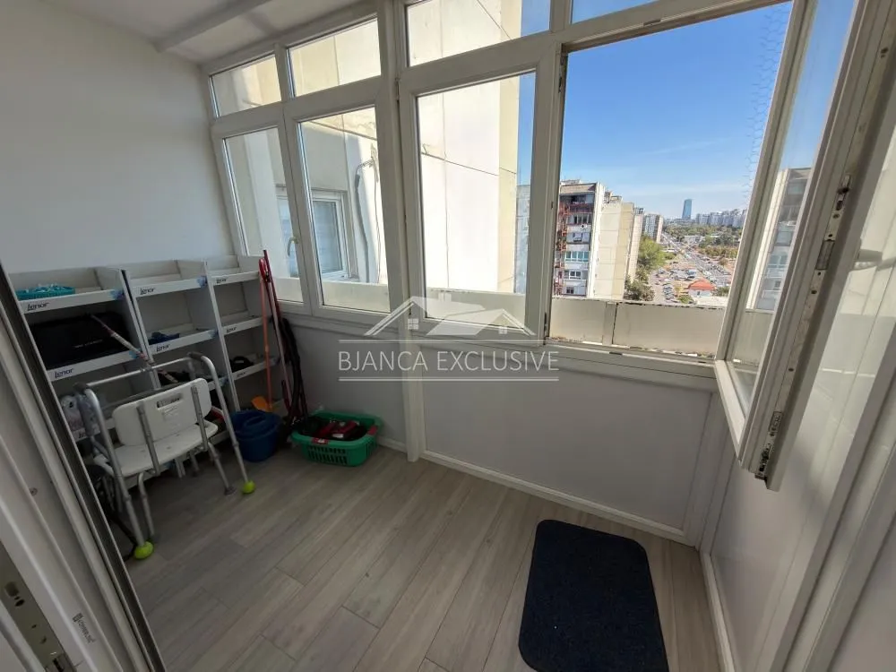 Zastakljeni balkon sa policama za odlaganje i pogledom na okolne zgrade.