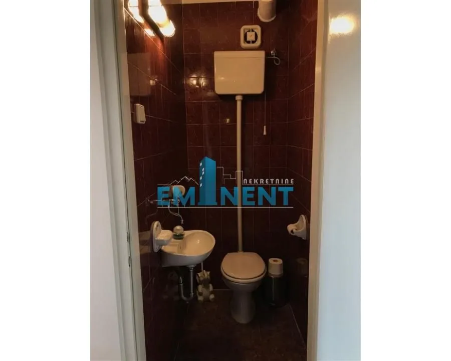 Small bathroom tiled with dark red tiles featuring a toilet and washbasin.