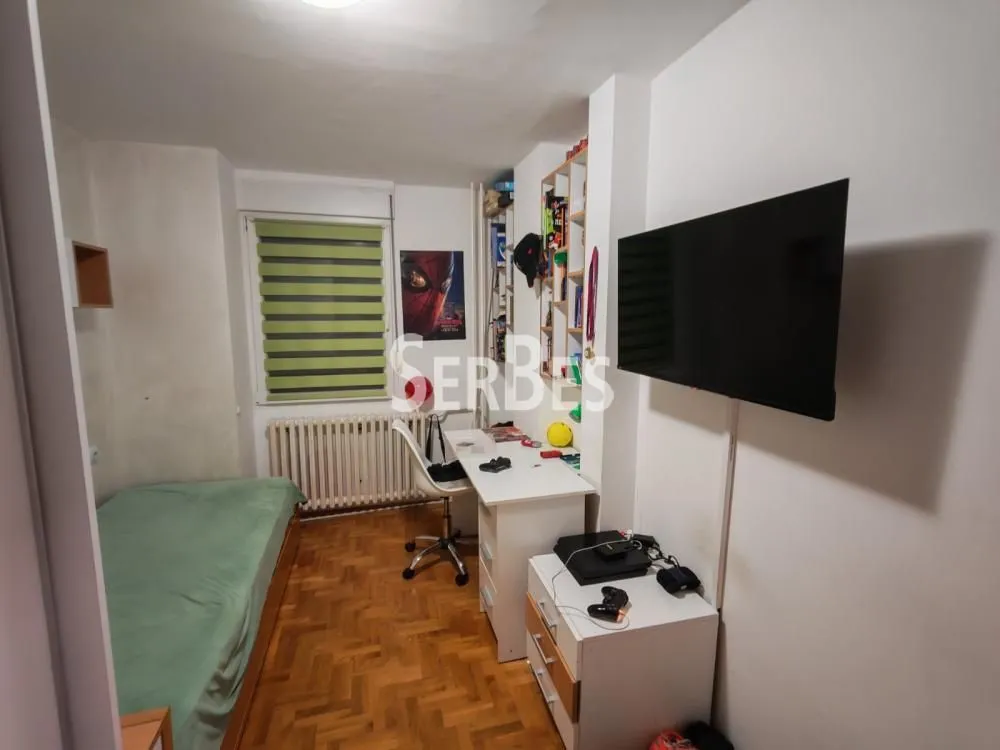 Dečja soba sa krevetom, radnim stolom i zidnim televizorom.