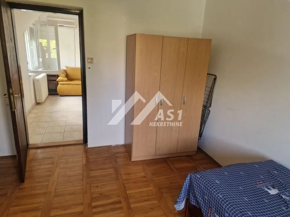Nameštena spavaća soba sa drvenim ormarom i pogledom na susednu prostoriju.